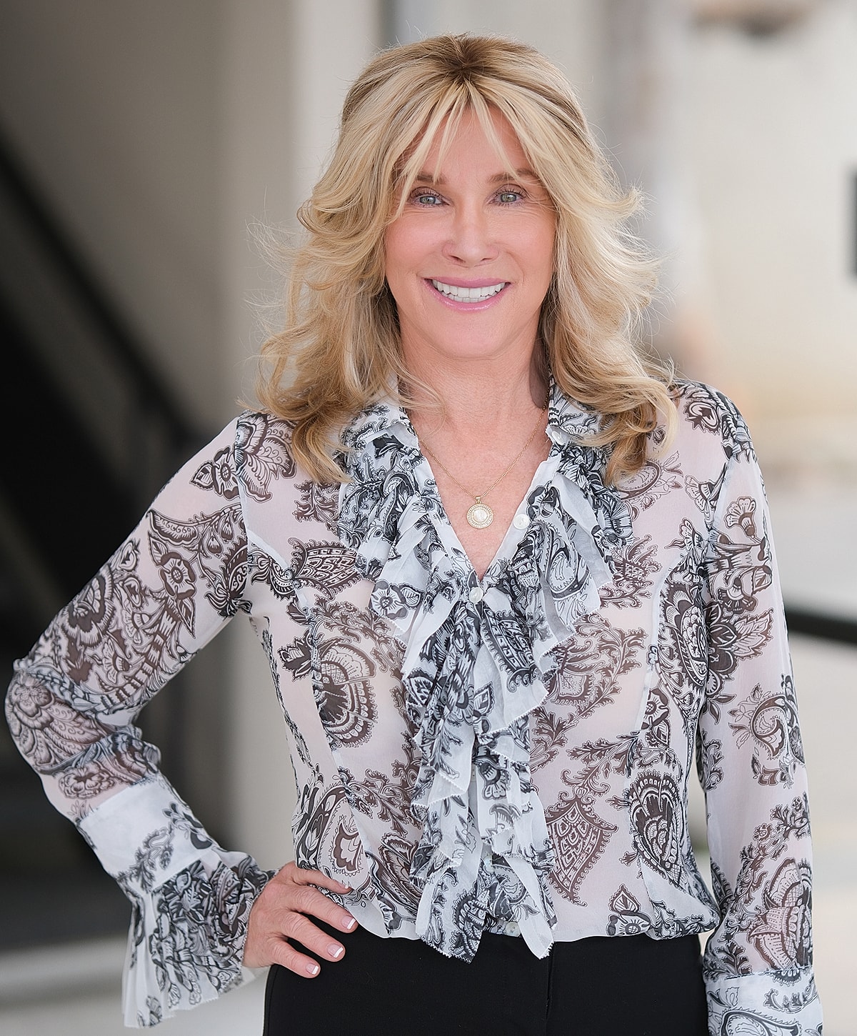 Woman smiling in patterned blouse, indoor setting.