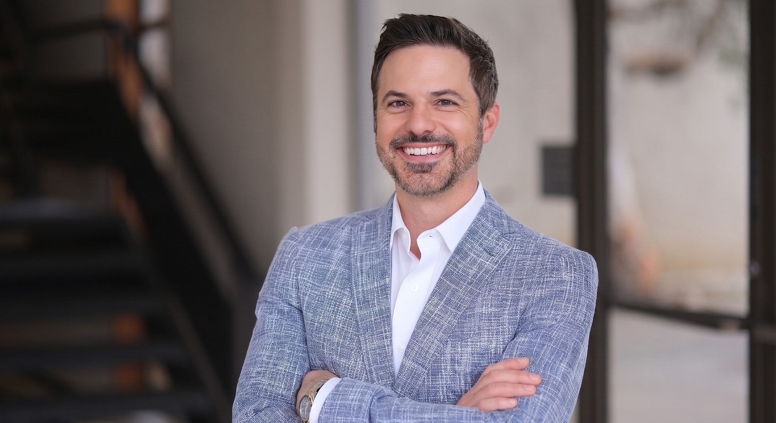 Smiling man in blazer with crossed arms.