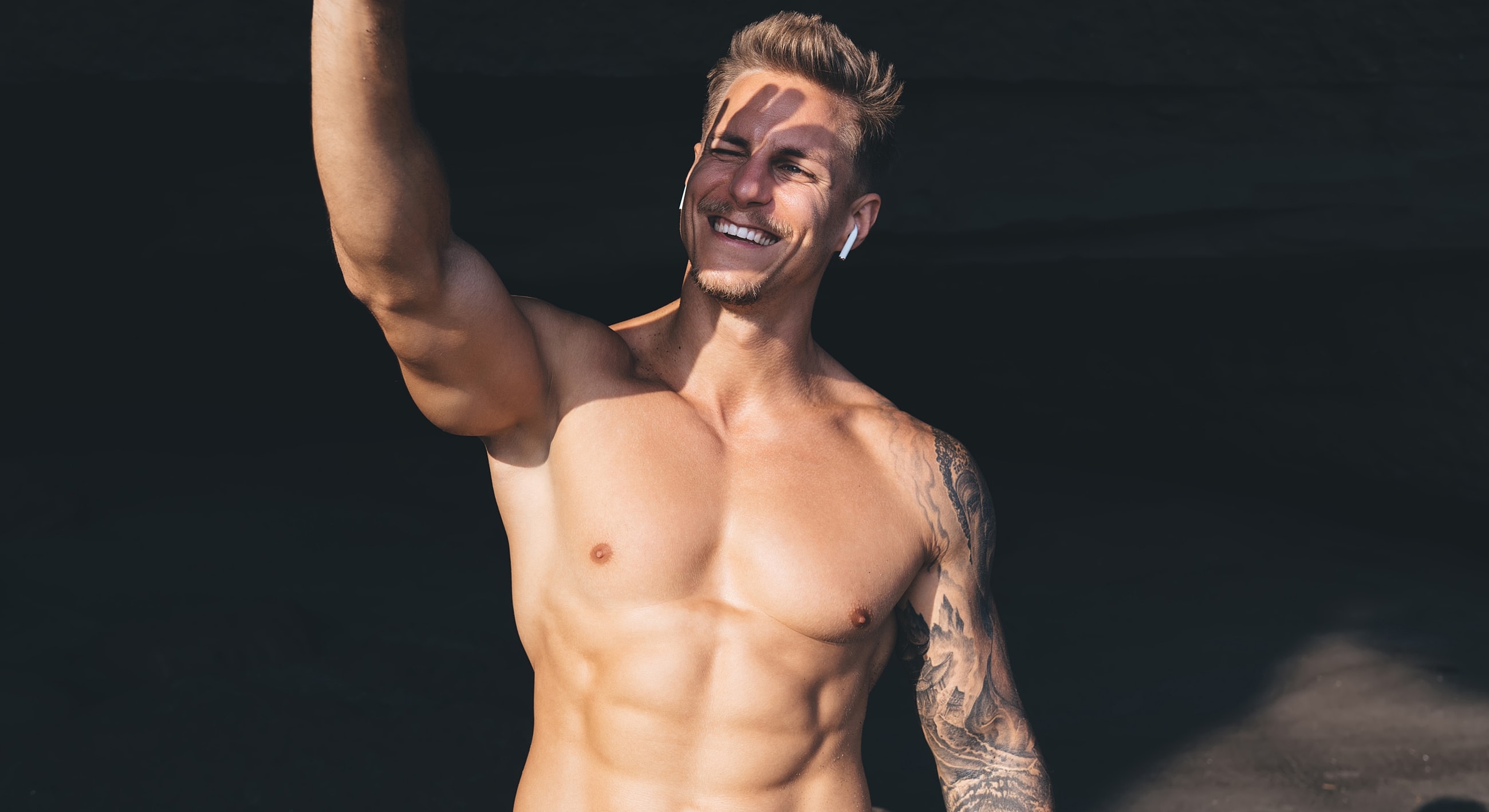 Smiling man with tattoo posing in sunlight.